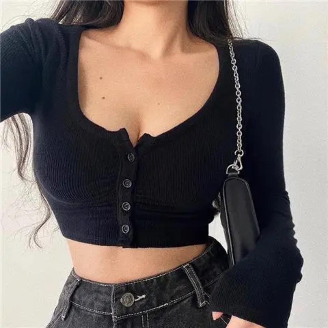 Person wearing a black ribbed crop top and holding a black handbag against a plain background
