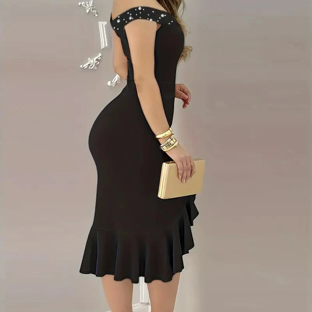 Black dress with shoulder embellishments and a gold clutch on a plain background