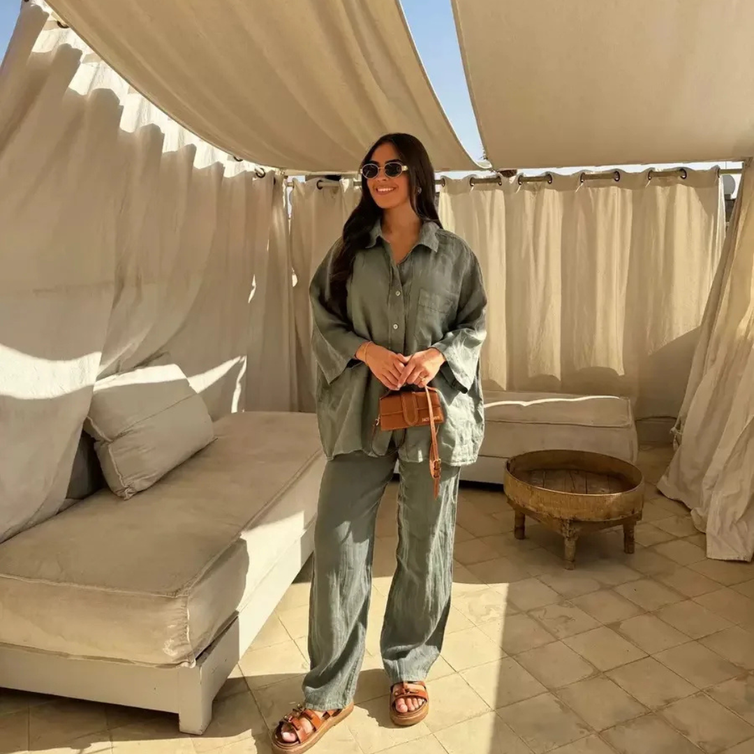 Woman in a Army Green Vanta Femme Structured 2-Piece Set outfit standing in a sunlit outdoor area with beige curtains and furniture.