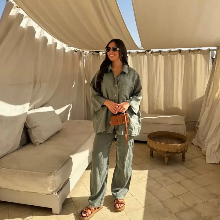 Woman in a Army Green Vanta Femme Structured 2-Piece Set outfit standing in a sunlit outdoor area with beige curtains and furniture.