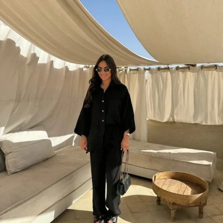 Woman in Black Vanta Femme Structured 2-Piece Set outfit standing in a stylish outdoor setting with beige curtains and furniture.