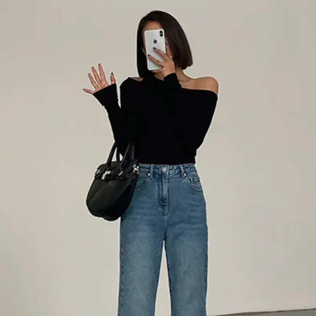 Person wearing a black off-shoulder top and blue jeans, holding a phone.