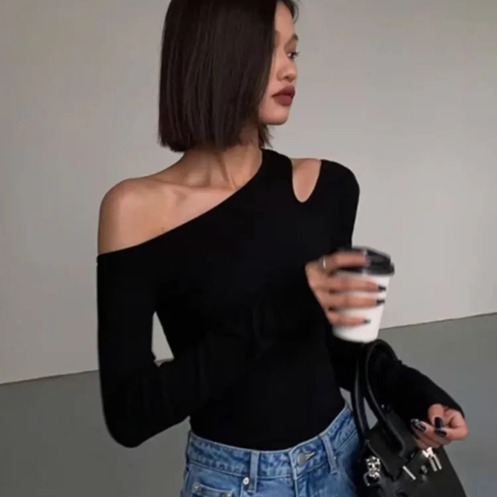 Woman wearing a black one-shoulder top and blue jeans, holding a coffee cup.