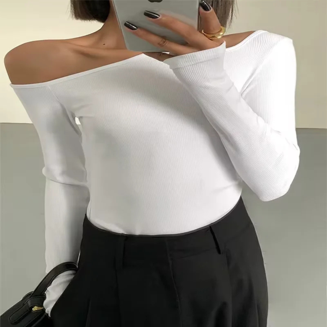 Person wearing a white off-shoulder long-sleeve top and black pants, holding a phone.