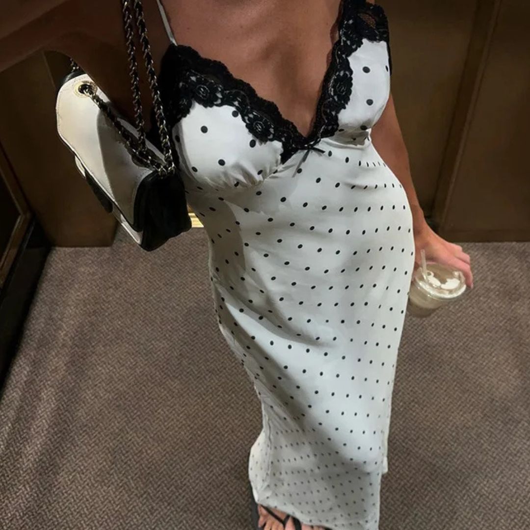 Person wearing a white dress with black polka dots and lace details, holding a handbag.