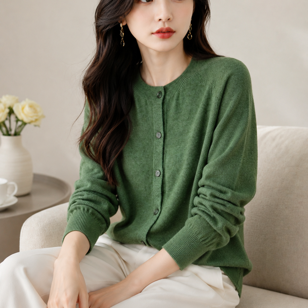 Woman wearing a green cardigan sitting on a couch in a cozy room.