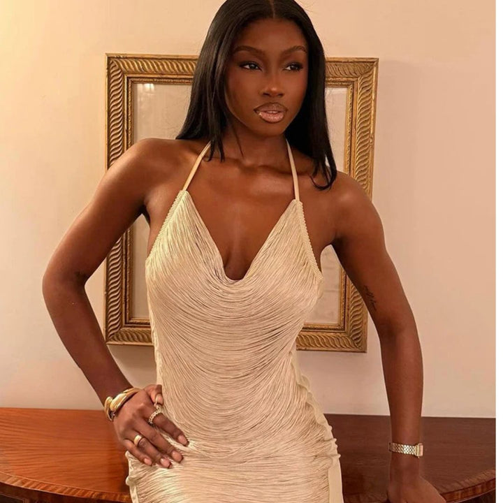 Woman wearing a beige beaded dress in an indoor setting with a framed picture in the background.